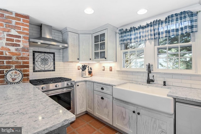 kitchen with sink, light stone countertops, stainless steel range with gas stovetop, and wall chimney exhaust hood