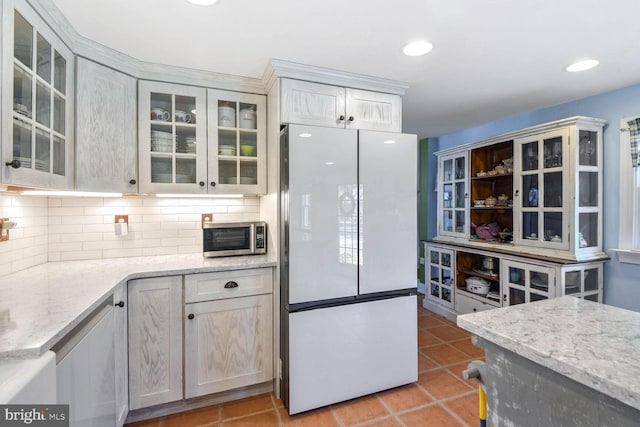 kitchen with light tile patterned flooring, white fridge, backsplash, and light stone counters