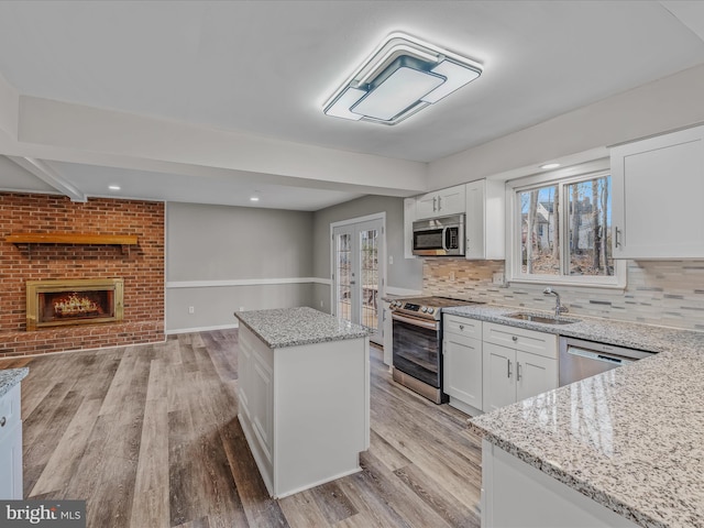 kitchen featuring sink, white cabinetry, appliances with stainless steel finishes, a kitchen island, and light stone countertops