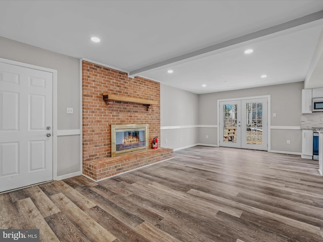 unfurnished living room featuring french doors, a fireplace, beam ceiling, and light hardwood / wood-style flooring