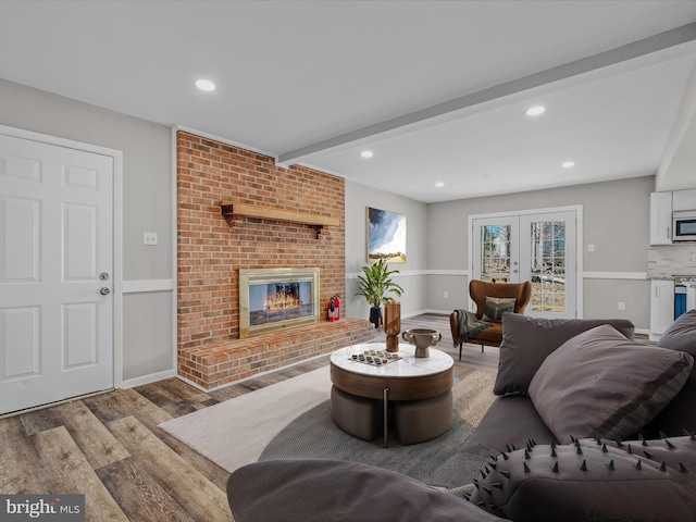 living room with beamed ceiling, french doors, a fireplace, and light hardwood / wood-style flooring