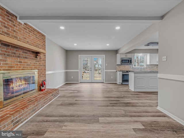 unfurnished living room with a brick fireplace, sink, light hardwood / wood-style floors, and french doors