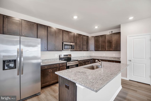 kitchen featuring sink, light hardwood / wood-style flooring, stainless steel appliances, light stone countertops, and a kitchen island with sink