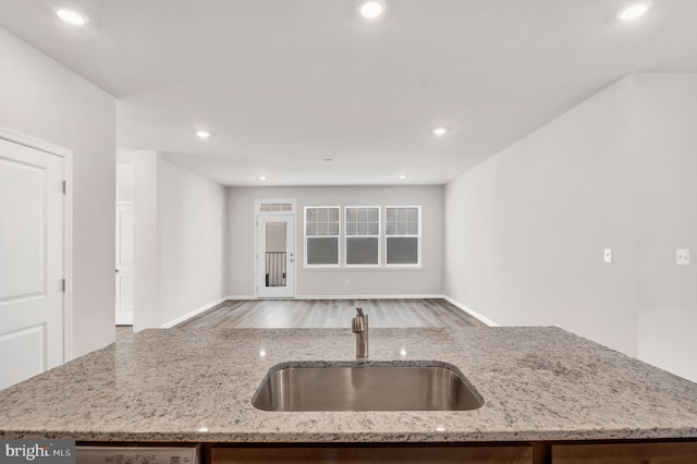 kitchen with dishwasher, light stone countertops, a kitchen island with sink, and sink