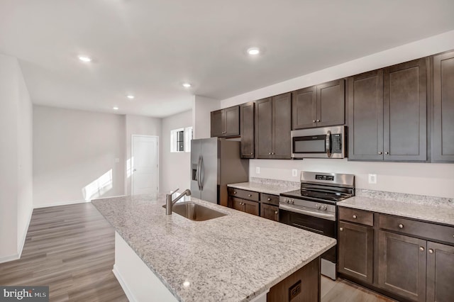 kitchen featuring sink, light hardwood / wood-style flooring, an island with sink, stainless steel appliances, and light stone countertops