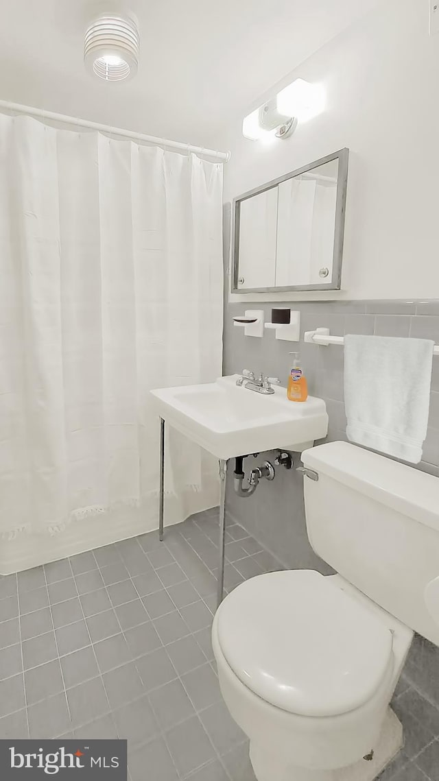 bathroom with toilet, tile patterned flooring, and tile walls