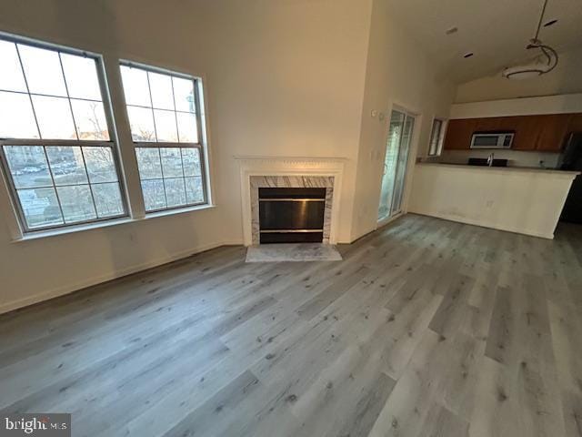 unfurnished living room featuring a high end fireplace, high vaulted ceiling, and light wood-type flooring