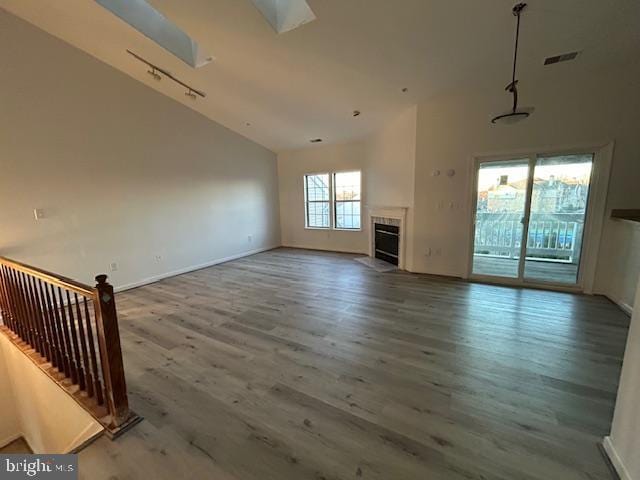 unfurnished living room featuring a skylight, high vaulted ceiling, rail lighting, and wood-type flooring