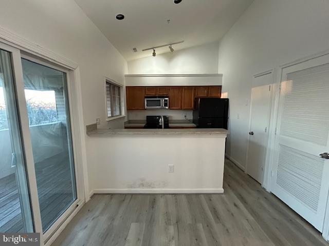 kitchen with lofted ceiling, light hardwood / wood-style flooring, black refrigerator, kitchen peninsula, and stove