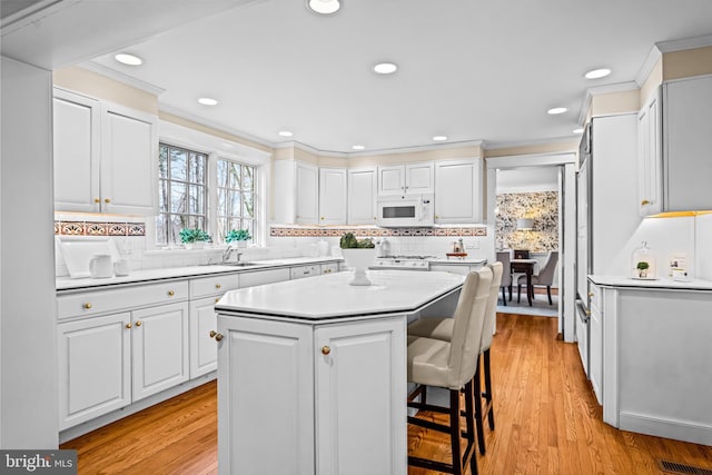 kitchen with a kitchen island, light wood-type flooring, white cabinets, and a kitchen bar