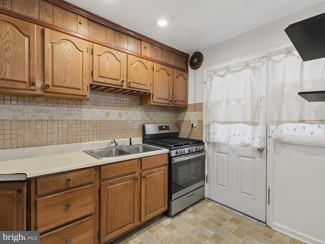 kitchen featuring a sink, light countertops, stainless steel gas range, backsplash, and brown cabinets