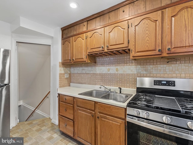 kitchen with a sink, light countertops, appliances with stainless steel finishes, backsplash, and stone finish floor