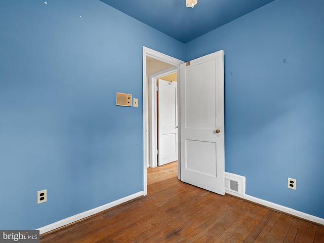 spare room with wood-type flooring, visible vents, and baseboards