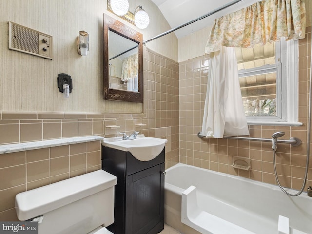 bathroom with wallpapered walls, wainscoting, toilet, vanity, and tile walls