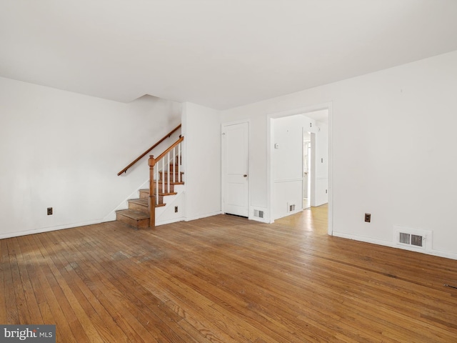 unfurnished living room with baseboards, visible vents, stairway, and hardwood / wood-style floors