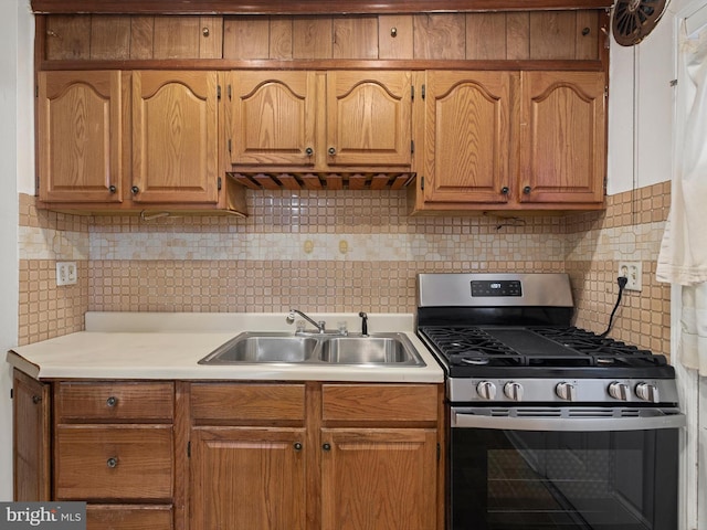 kitchen with stainless steel gas range oven, a sink, light countertops, decorative backsplash, and brown cabinetry