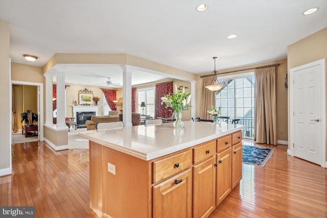 kitchen featuring hanging light fixtures, light wood-type flooring, a center island, and ornate columns