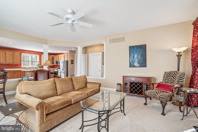 carpeted living room featuring ceiling fan, sink, and ornate columns