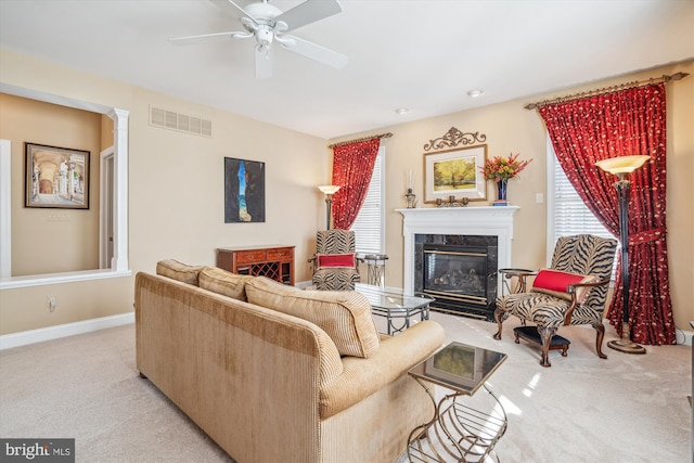 living room with a high end fireplace, light colored carpet, and ceiling fan