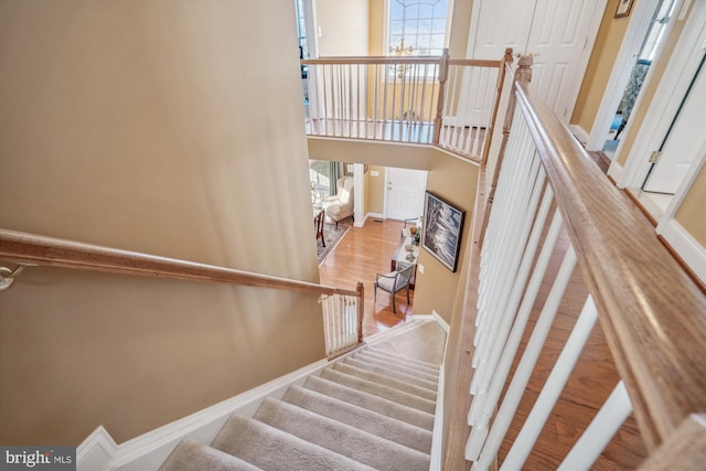 stairway featuring an inviting chandelier, a towering ceiling, and wood-type flooring