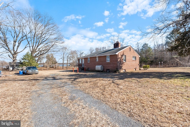 view of side of property featuring brick siding, a chimney, a lawn, driveway, and heating fuel