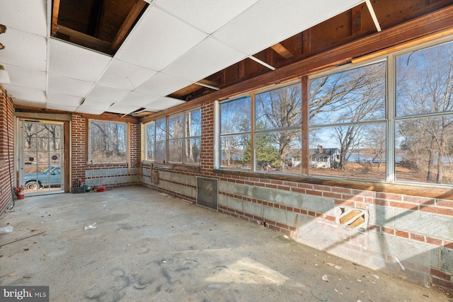 miscellaneous room featuring a sunroom, brick wall, unfinished concrete flooring, and a drop ceiling