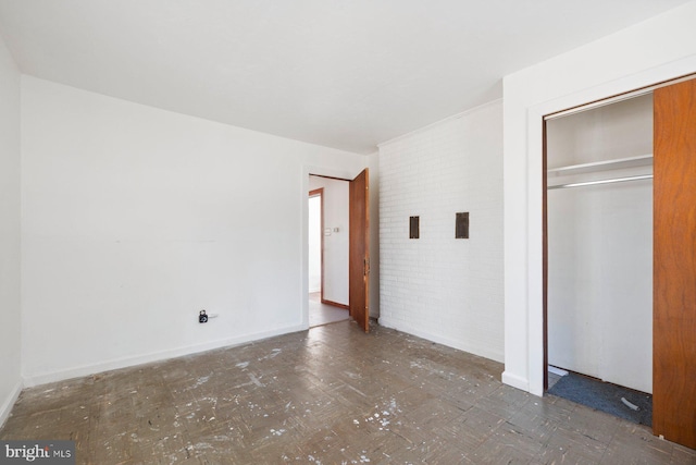 unfurnished bedroom featuring brick wall, dark floors, a closet, and baseboards