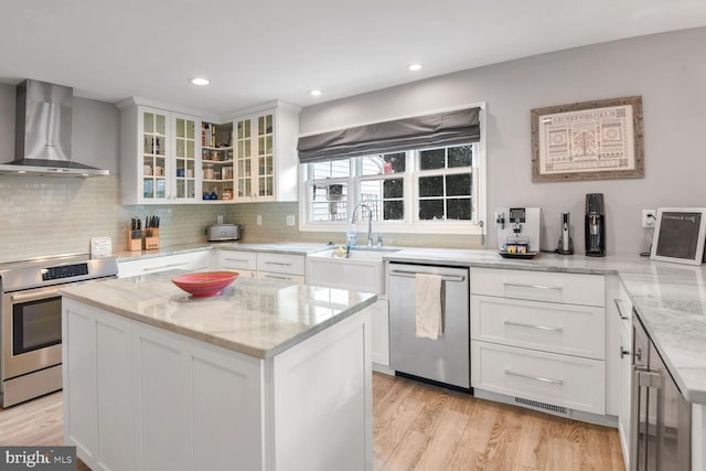 kitchen with white cabinetry, stainless steel appliances, a center island, and wall chimney range hood