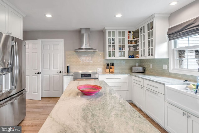 kitchen with white cabinetry, appliances with stainless steel finishes, wall chimney exhaust hood, and light stone counters