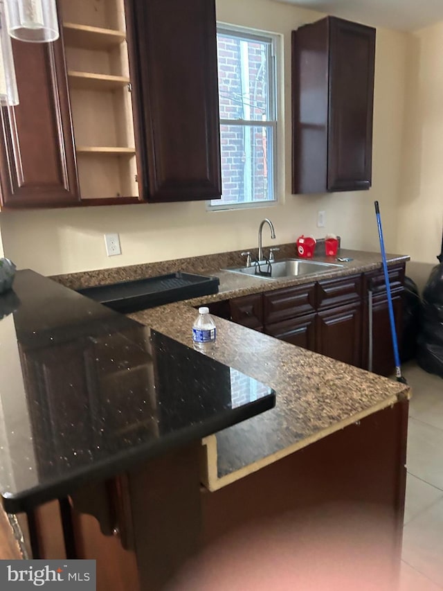 kitchen with dark stone counters, sink, dark brown cabinets, and light tile patterned floors