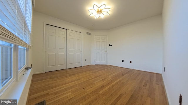 unfurnished bedroom with light wood-type flooring, visible vents, and a closet