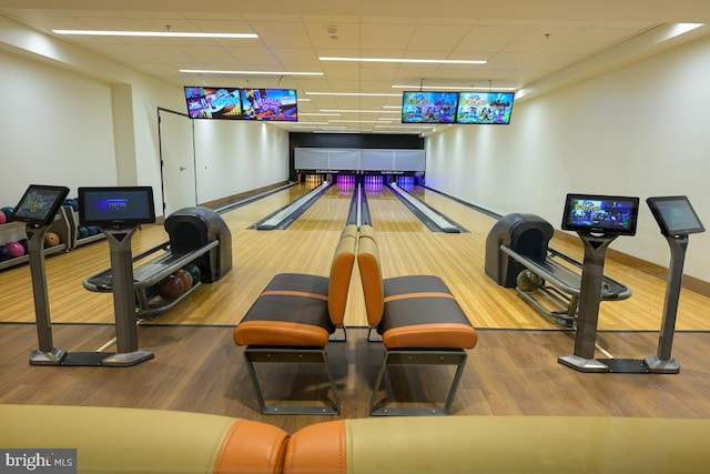 rec room with a drop ceiling, baseboards, wood finished floors, and bowling