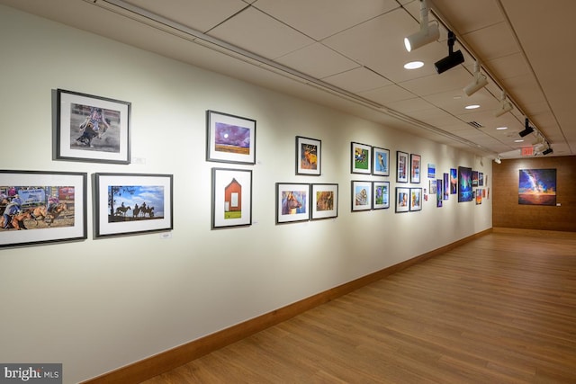 hall featuring track lighting, wood finished floors, and baseboards