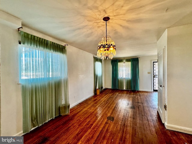 spare room with dark wood-type flooring and a notable chandelier