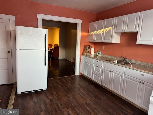 kitchen with sink, white cabinetry, dark hardwood / wood-style floors, light stone counters, and white fridge