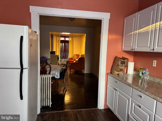 kitchen with radiator, dark hardwood / wood-style floors, light stone counters, white cabinets, and white fridge