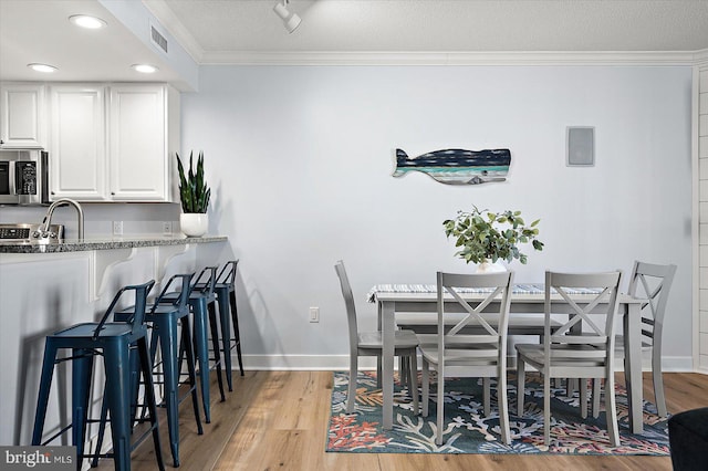 dining room featuring sink, crown molding, and light wood-type flooring