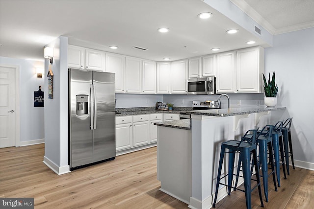 kitchen featuring white cabinetry, stainless steel appliances, kitchen peninsula, and dark stone countertops