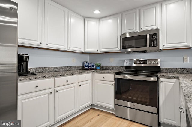 kitchen featuring dark stone countertops, appliances with stainless steel finishes, light hardwood / wood-style flooring, and white cabinets