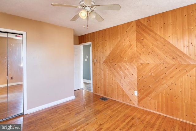 spare room with wood-type flooring, wooden walls, ceiling fan, and a textured ceiling