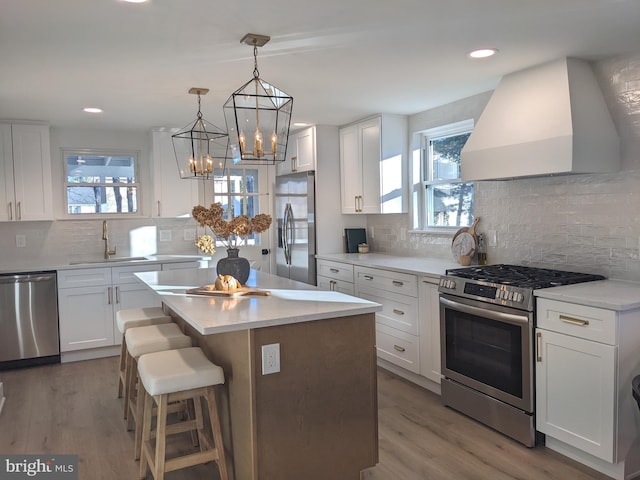 kitchen with sink, appliances with stainless steel finishes, a kitchen island, custom range hood, and white cabinets