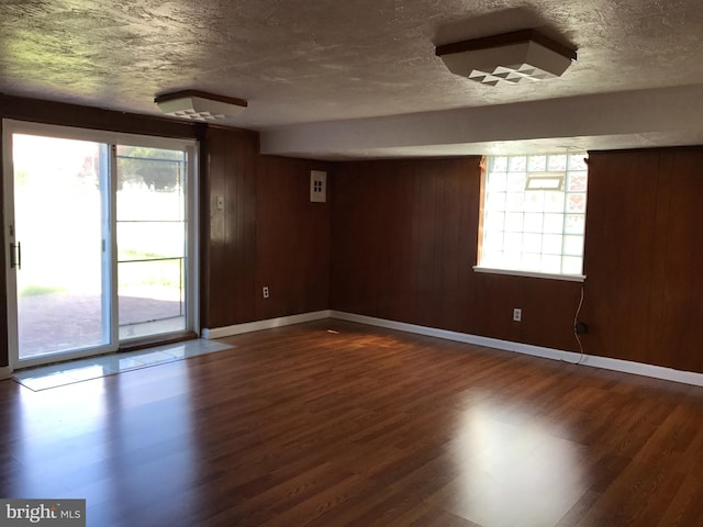 unfurnished room with dark hardwood / wood-style flooring, wooden walls, and a textured ceiling