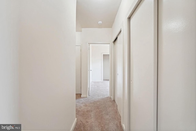 hallway featuring light carpet and baseboards