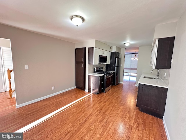 kitchen with dark brown cabinetry, sink, an inviting chandelier, appliances with stainless steel finishes, and light hardwood / wood-style floors