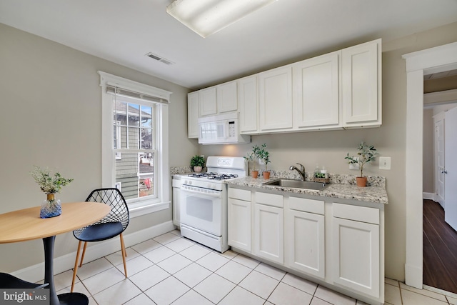 kitchen with white cabinetry, sink, light tile patterned floors, light stone countertops, and white appliances