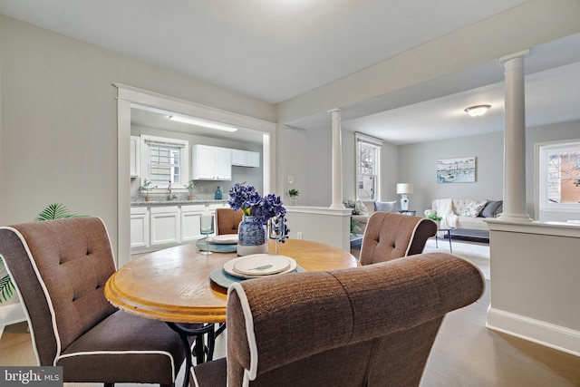 dining space featuring sink, light wood-type flooring, and ornate columns