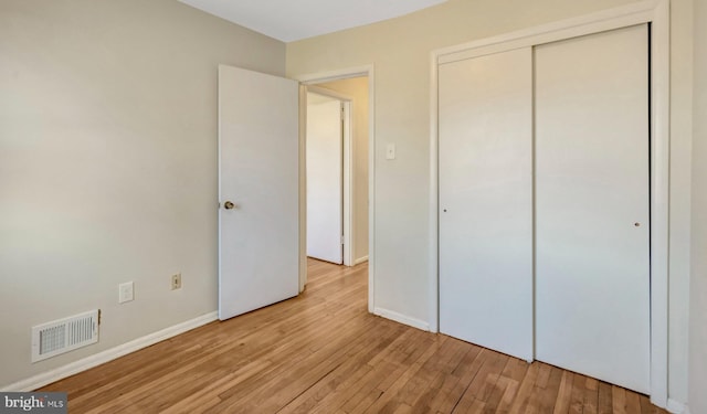 unfurnished bedroom with baseboards, light wood-style flooring, visible vents, and a closet