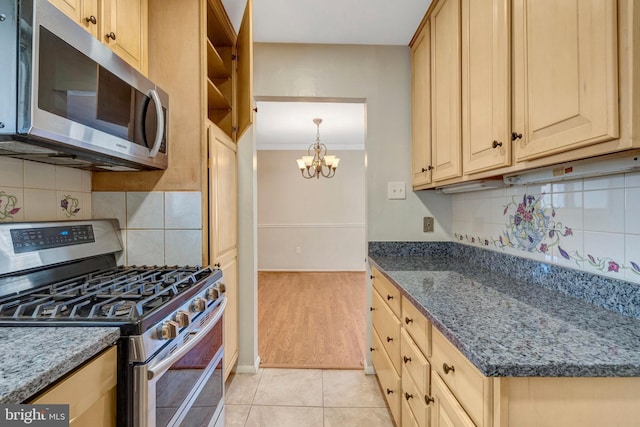 kitchen featuring dark stone counters, stainless steel appliances, crown molding, light brown cabinets, and light tile patterned flooring