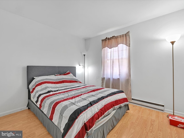 bedroom with baseboards, a baseboard heating unit, and wood finished floors