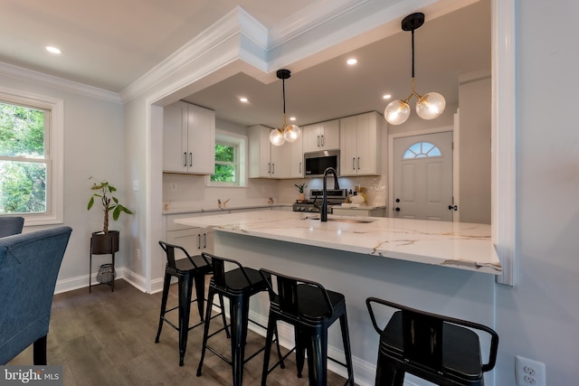 kitchen featuring appliances with stainless steel finishes, light stone counters, ornamental molding, white cabinets, and decorative light fixtures